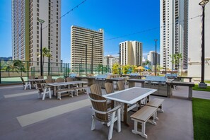 Une terrasse extérieure avec des tables et des chaises, des barbecues et une vue sur de hauts immeubles.