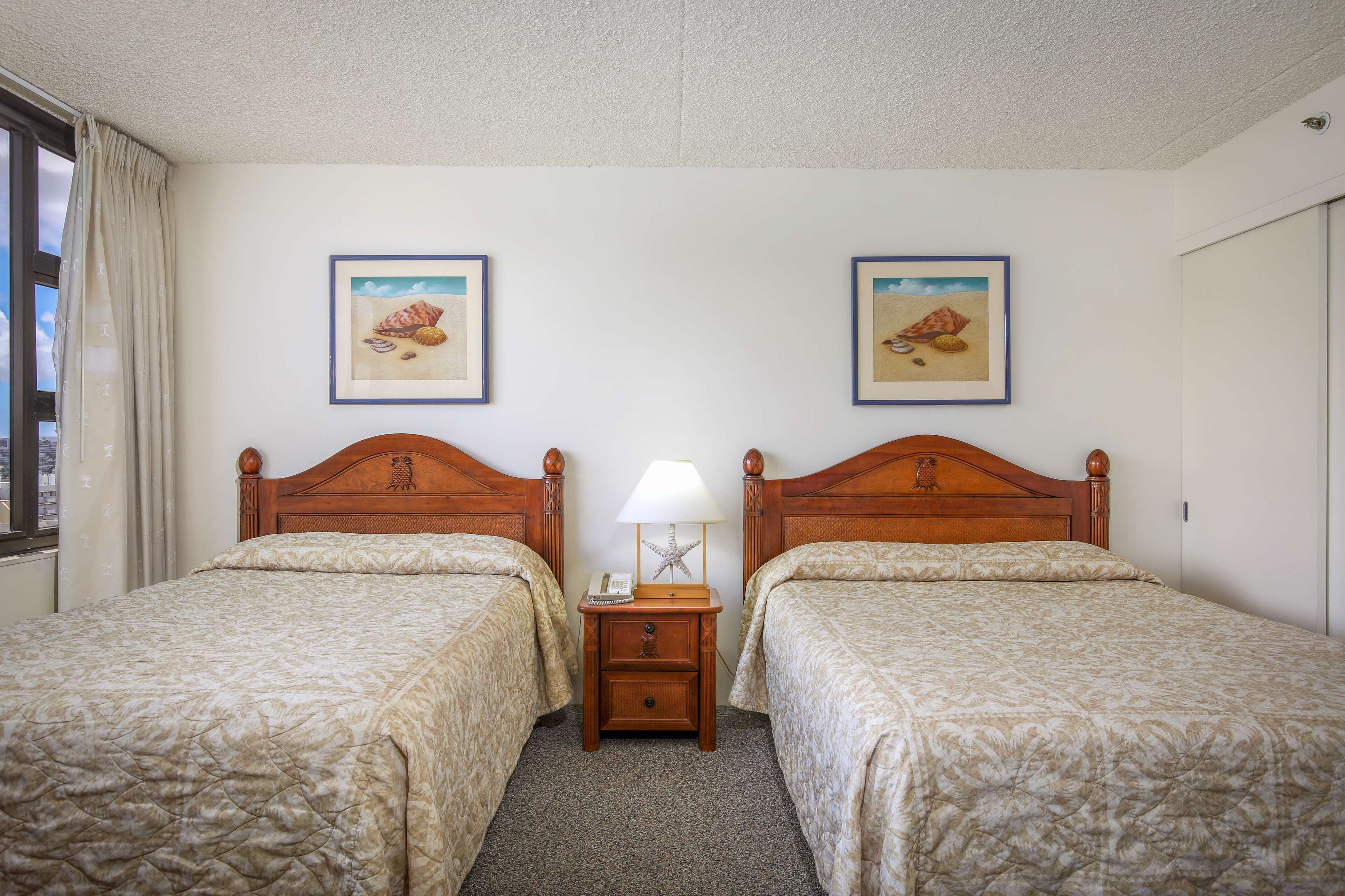 Una habitación de hotel con dos camas, una mesita de noche con lámpara y cuadros en la pared.