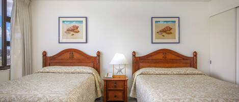 Una habitación de hotel con dos camas, una mesita de noche con lámpara y cuadros en la pared.