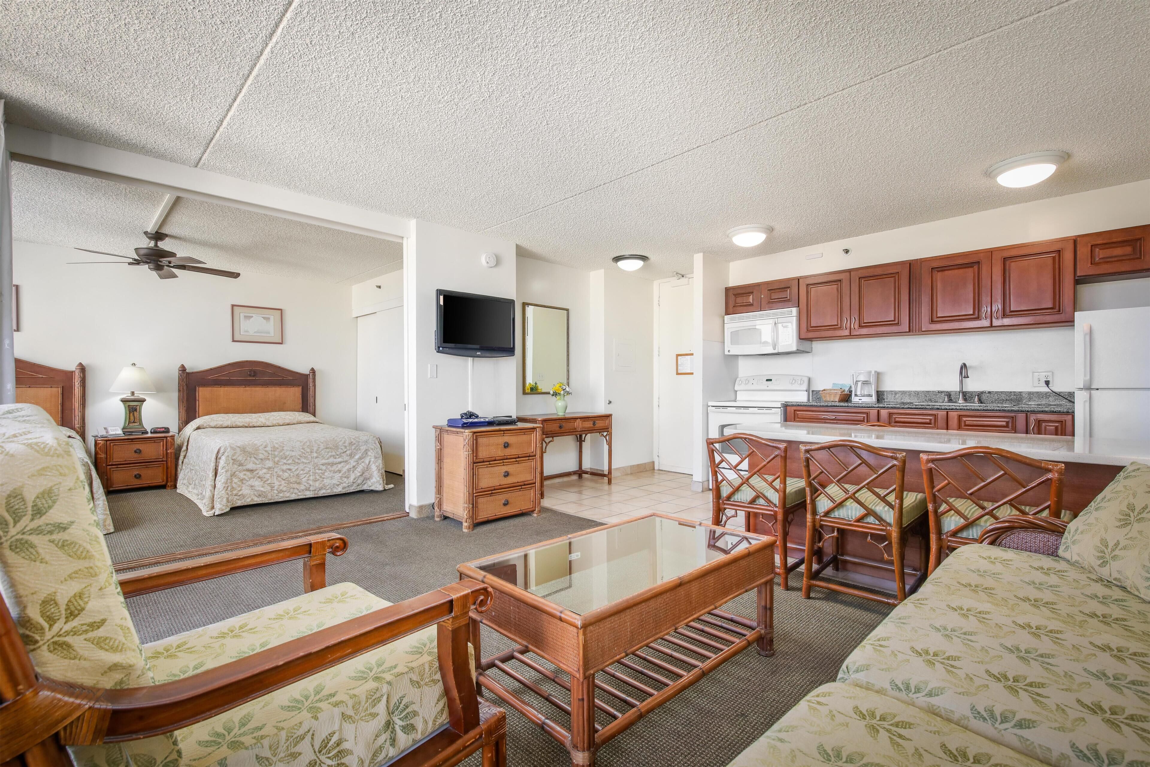 A compact room with a bed, a desk, a kitchenette, and a seating area with a glass table.