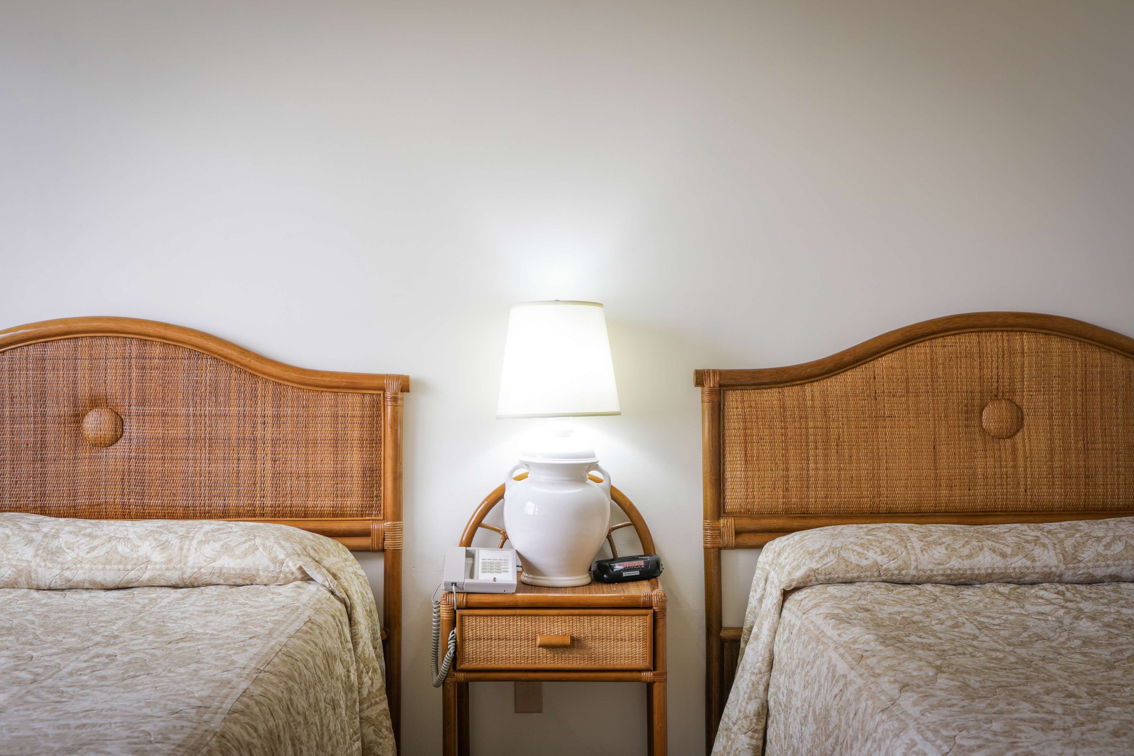 Two single beds with headboards, a bedside table with a lamp, a phone, and a small electronic device.