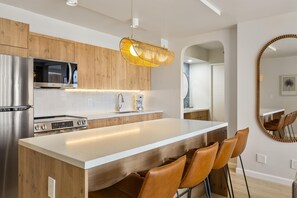 A modern kitchen with a central island, stainless steel appliances, and a pendant light. - Aston at the Waikiki Banyan (Honolulu)