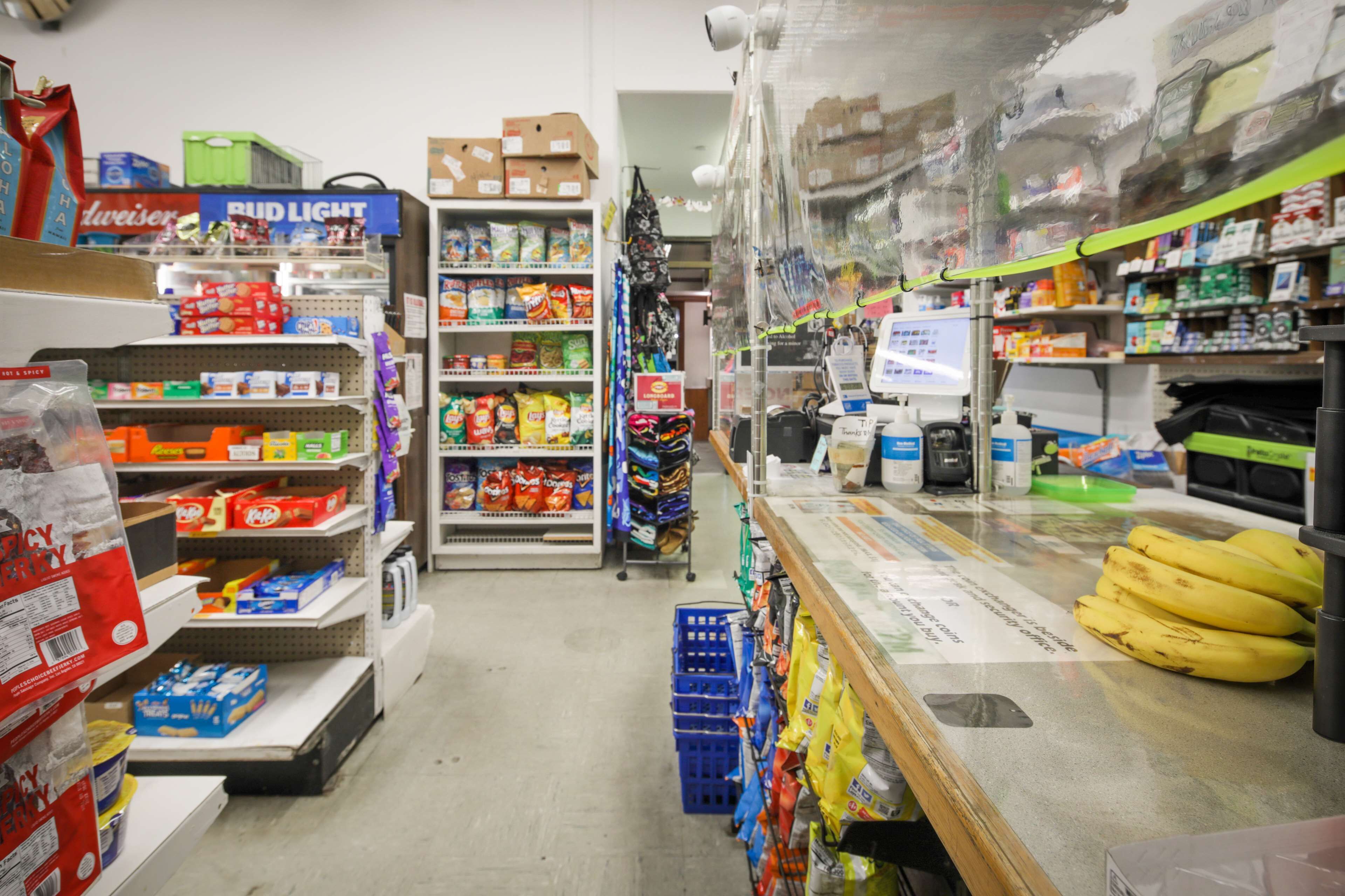 L’intérieur d’une épicerie, avec des étagères remplies de divers produits alimentaires, un comptoir de caisse et une caméra de surveillance.