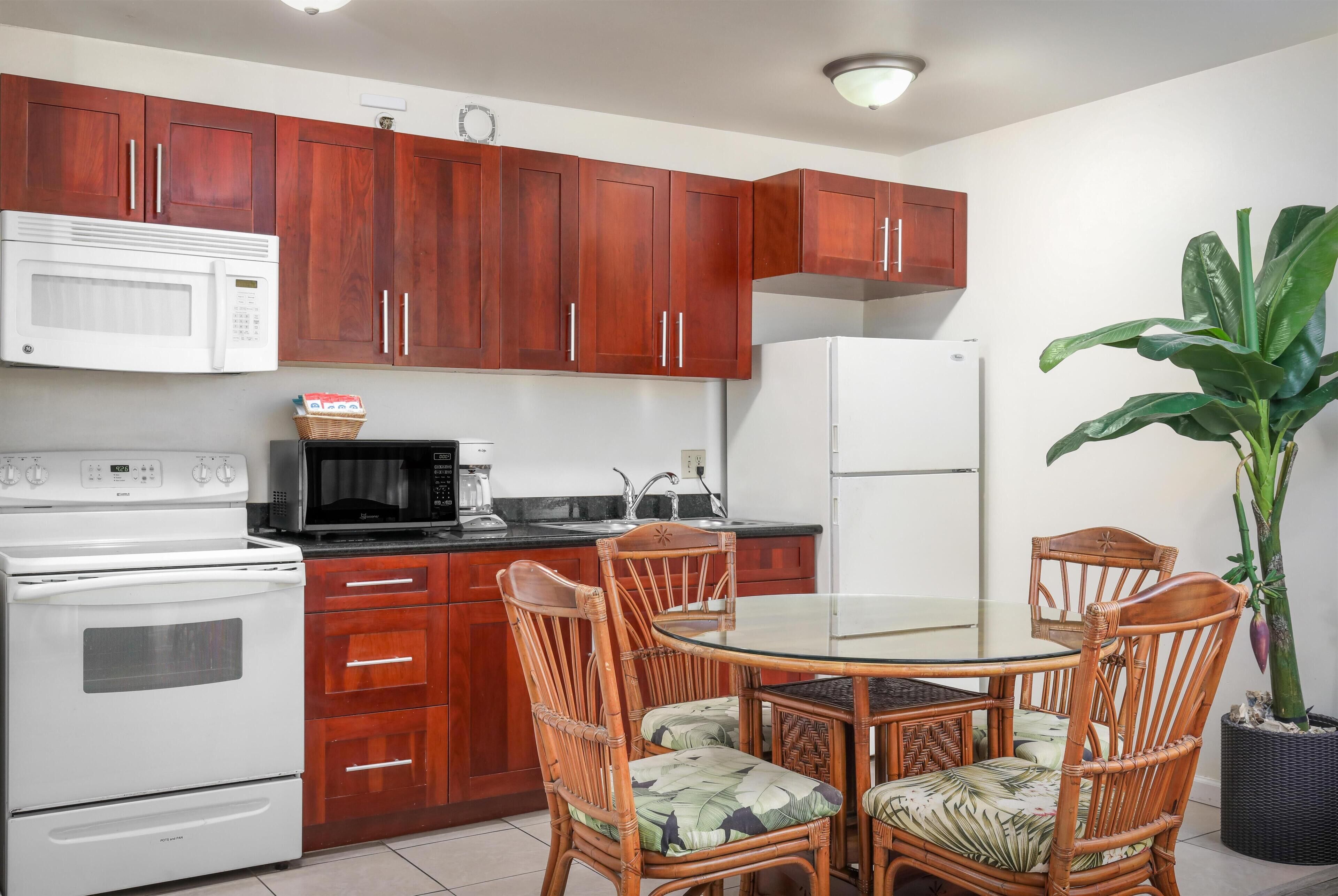 A kitchen with wooden cabinets, a white stove, a microwave, and a refrigerator. There is a dining table with chairs and a potted plant.