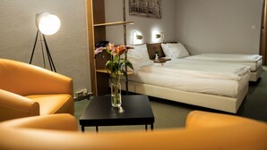 Een hotelkamer met een bed, een stoel, een klein tafeltje met een bloevas en een aan de muur hangend schilderij.