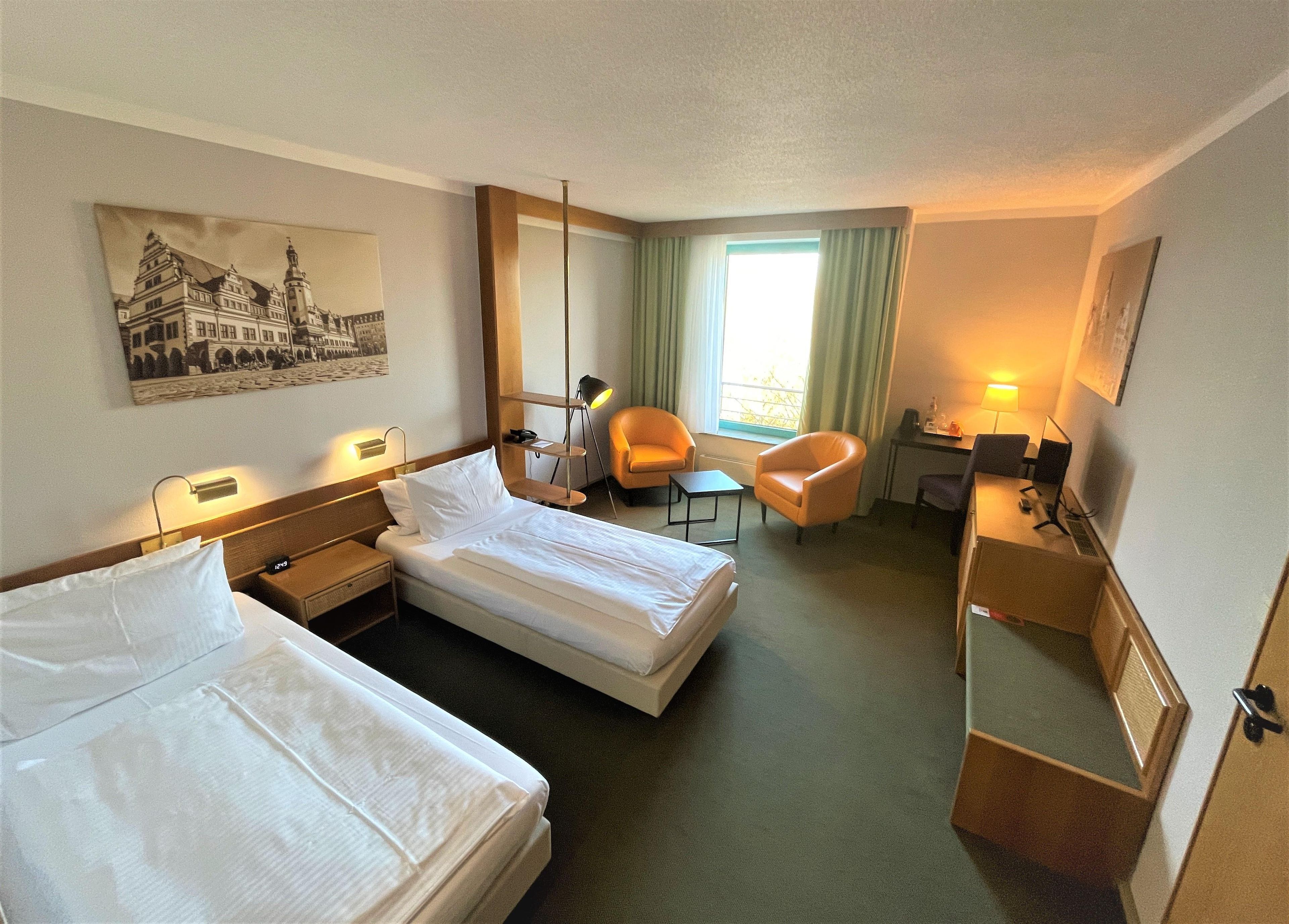 A hotel room with two beds, a desk, a chair, a lamp, and a painting on the wall.