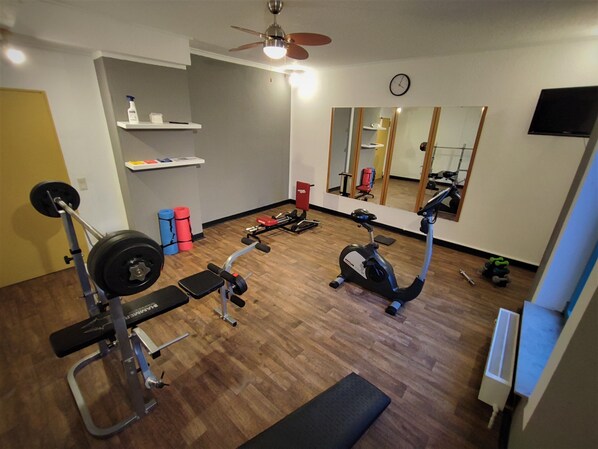 A gym with a ceiling fan, a treadmill, a stationary bike, and a bench.