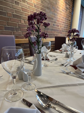 A dining table set with wine glasses, cutlery, and a vase with purple flowers.