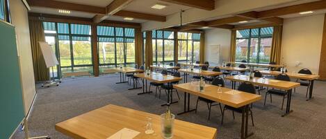 A conference room with multiple tables and chairs, large windows, and a whiteboard.