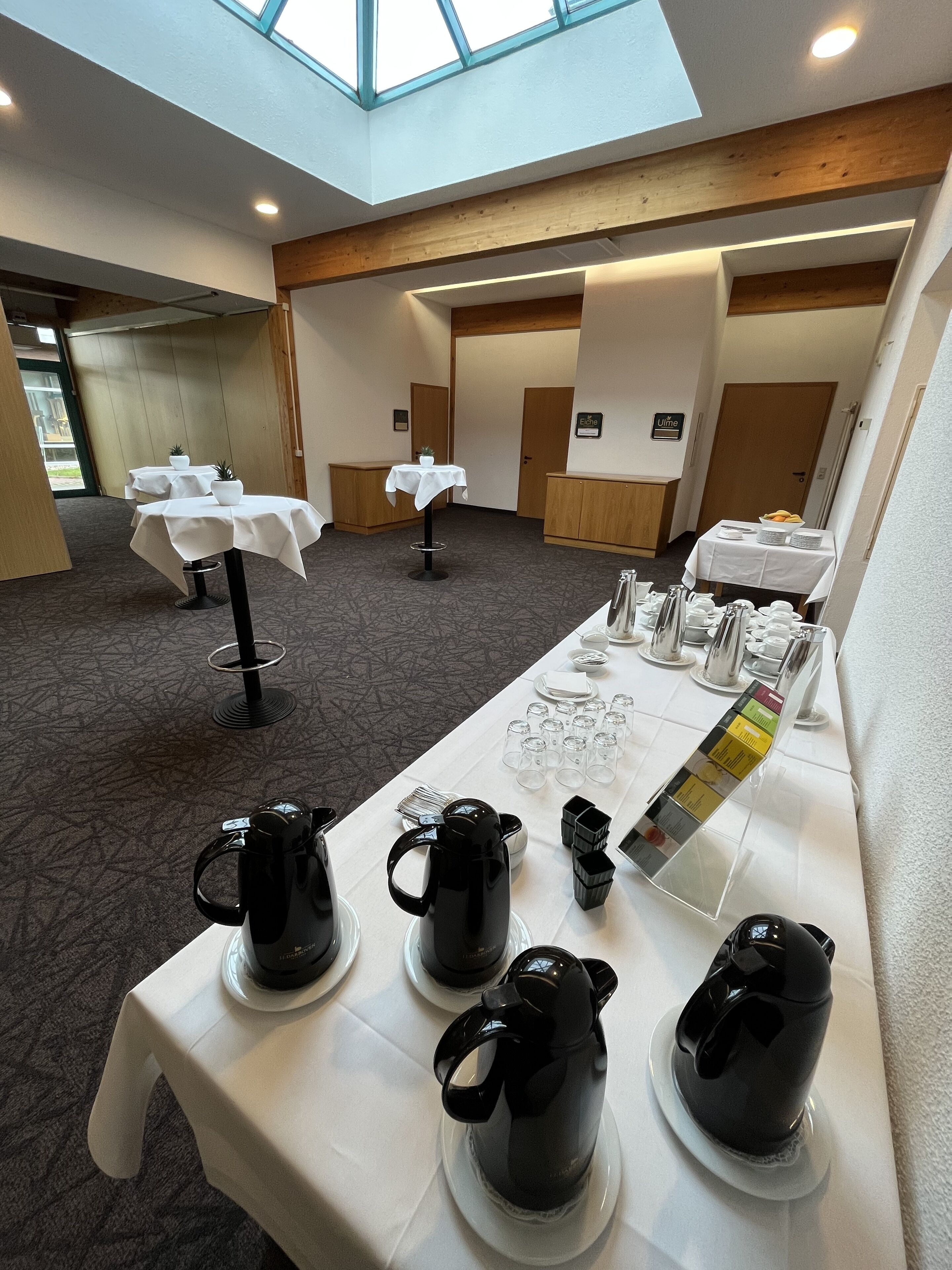 A conference room with tables set for a meeting, equipped with coffee pots and glassware.