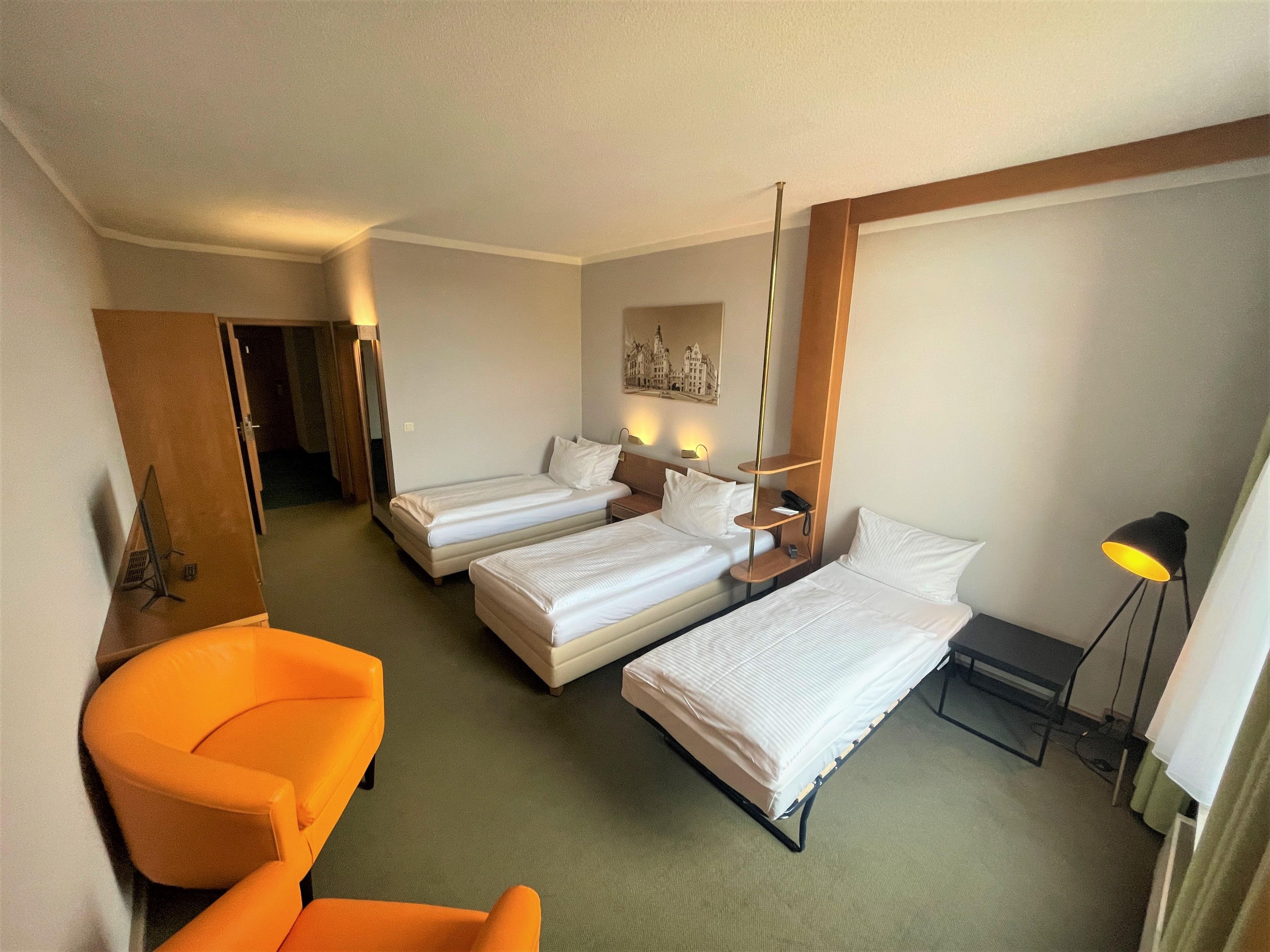 A hotel room with two single beds, a desk, a chair, a lamp, and a painting on the wall.