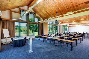 Un salón de conferencias con mesas y sillas, ventanas amplias y techo de madera.