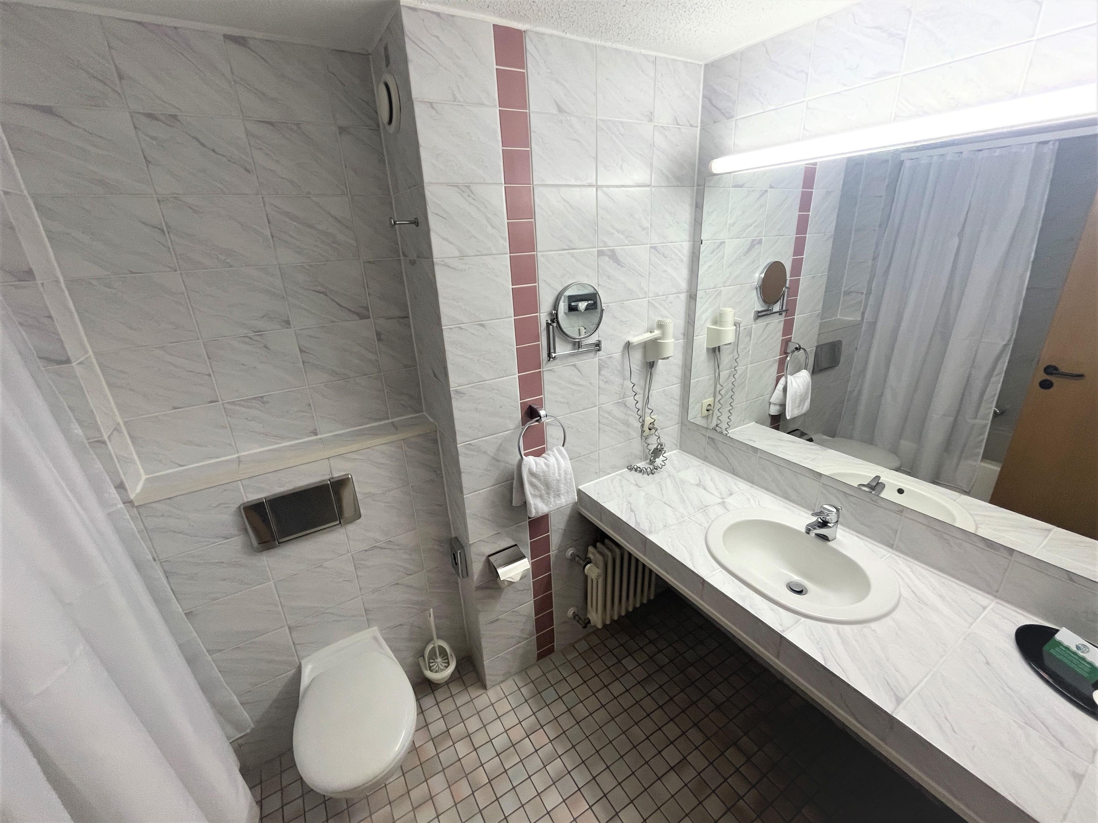 A bathroom with a toilet, sink, mirror, towel rack, and shower area.