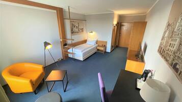 Habitación de hotel con cama, escritorio, silla, mesita, lámpara y un cuadro en la pared.