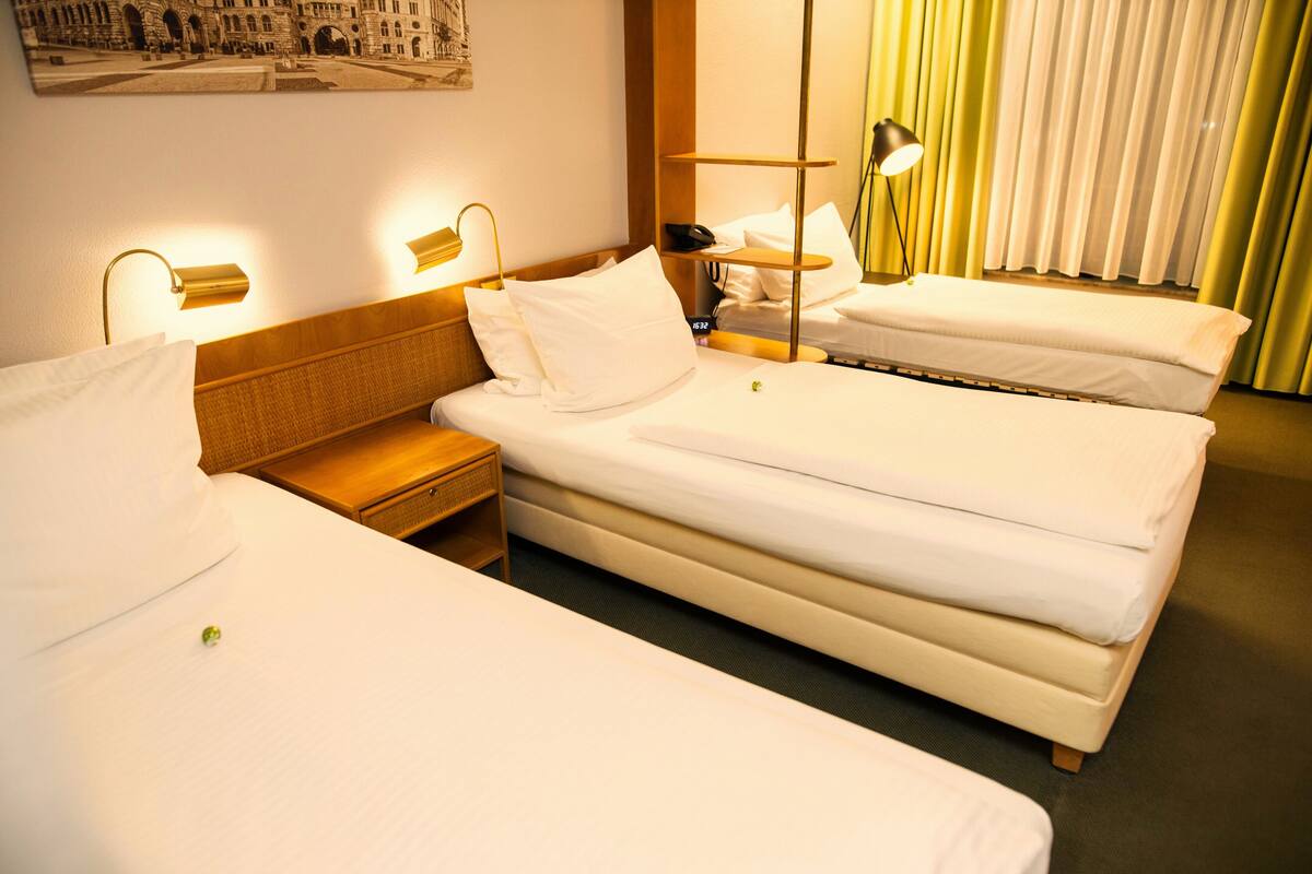 Una habitación de hotel con dos camas individuales, una mesita de noche de madera, una lámpara y un teléfono instalado en la pared.