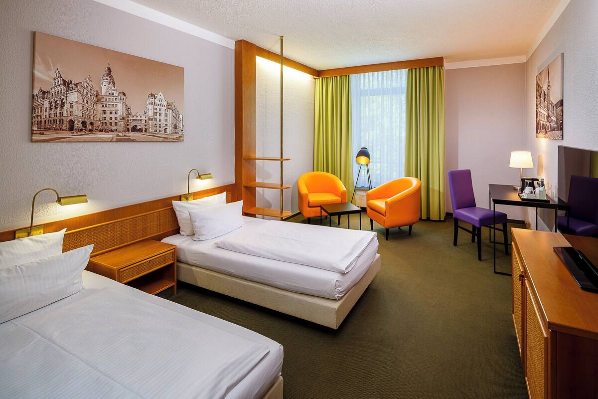 Habitación de hotel con dos camas, un escritorio, una silla, una lámpara y un cuadro en la pared.
