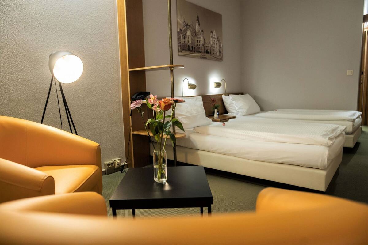 Una habitación de hotel con cama, escritorio, silla y un jarrón con flores.
