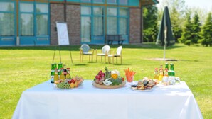 Een picknickopstelling met eten en drinken op een tafel, voor een gebouw met grote ramen en een bakstenen gevel.