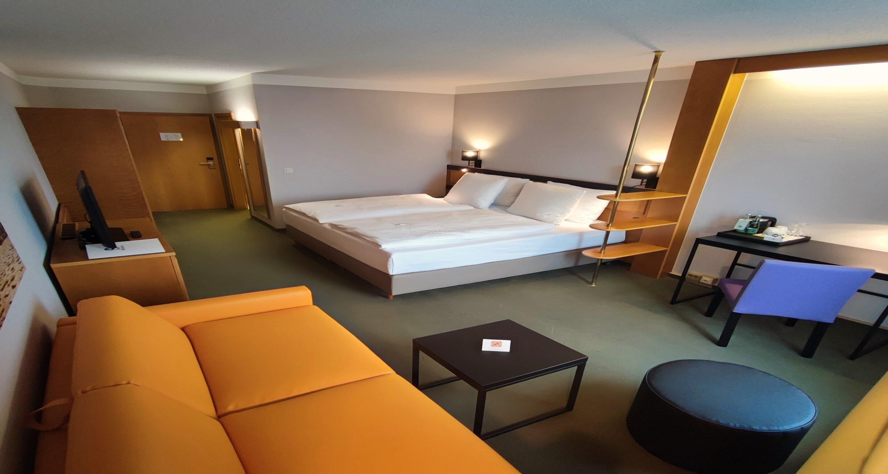 A hotel room with a bed, a desk, a chair, a sofa, and a small table.