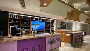 Zona de bar con mostrador, estantes llenos de botellas, vasos y una pantalla de televisión.