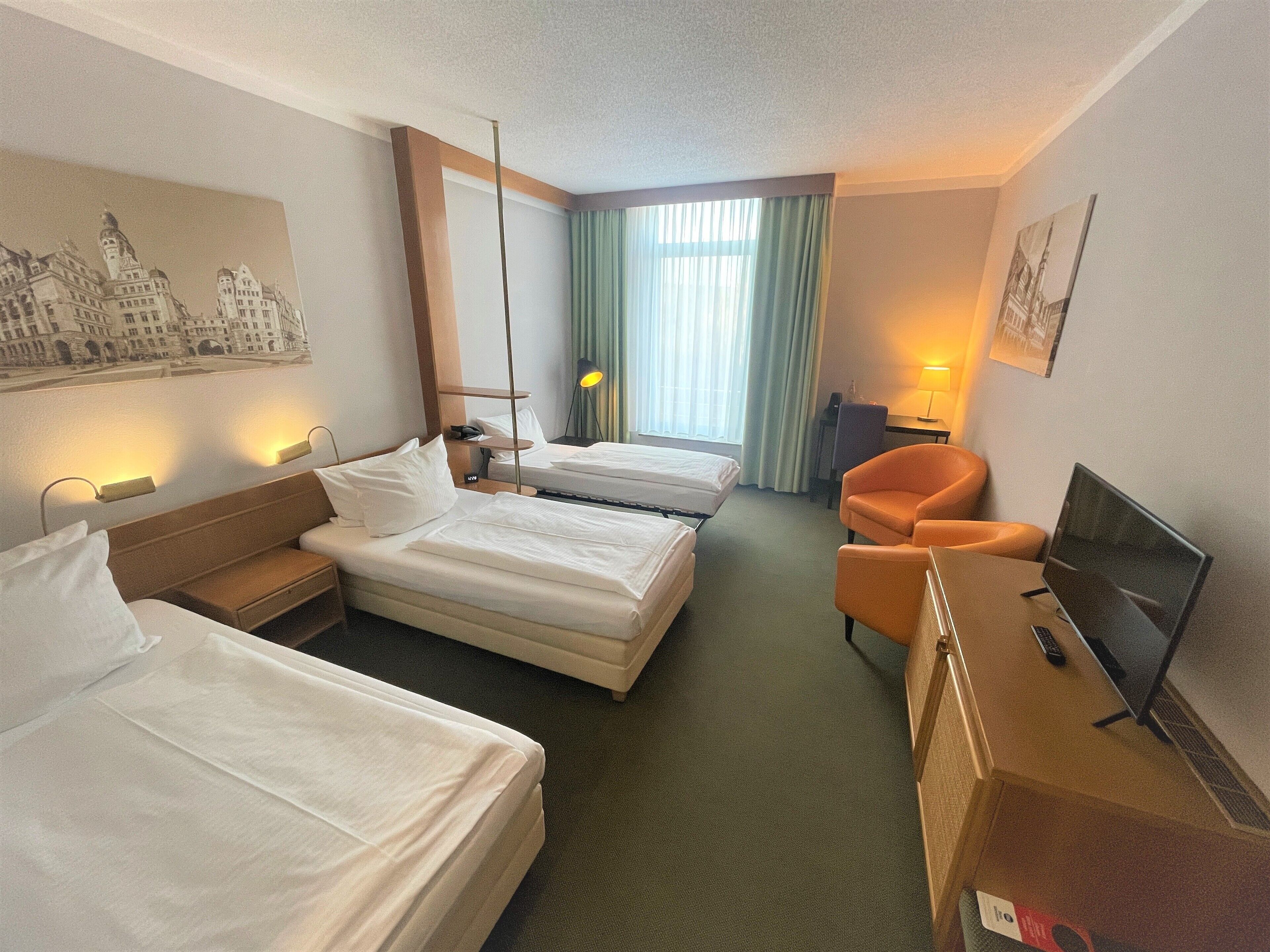 A hotel room with two beds, a desk, a chair, a TV, and a lamp.