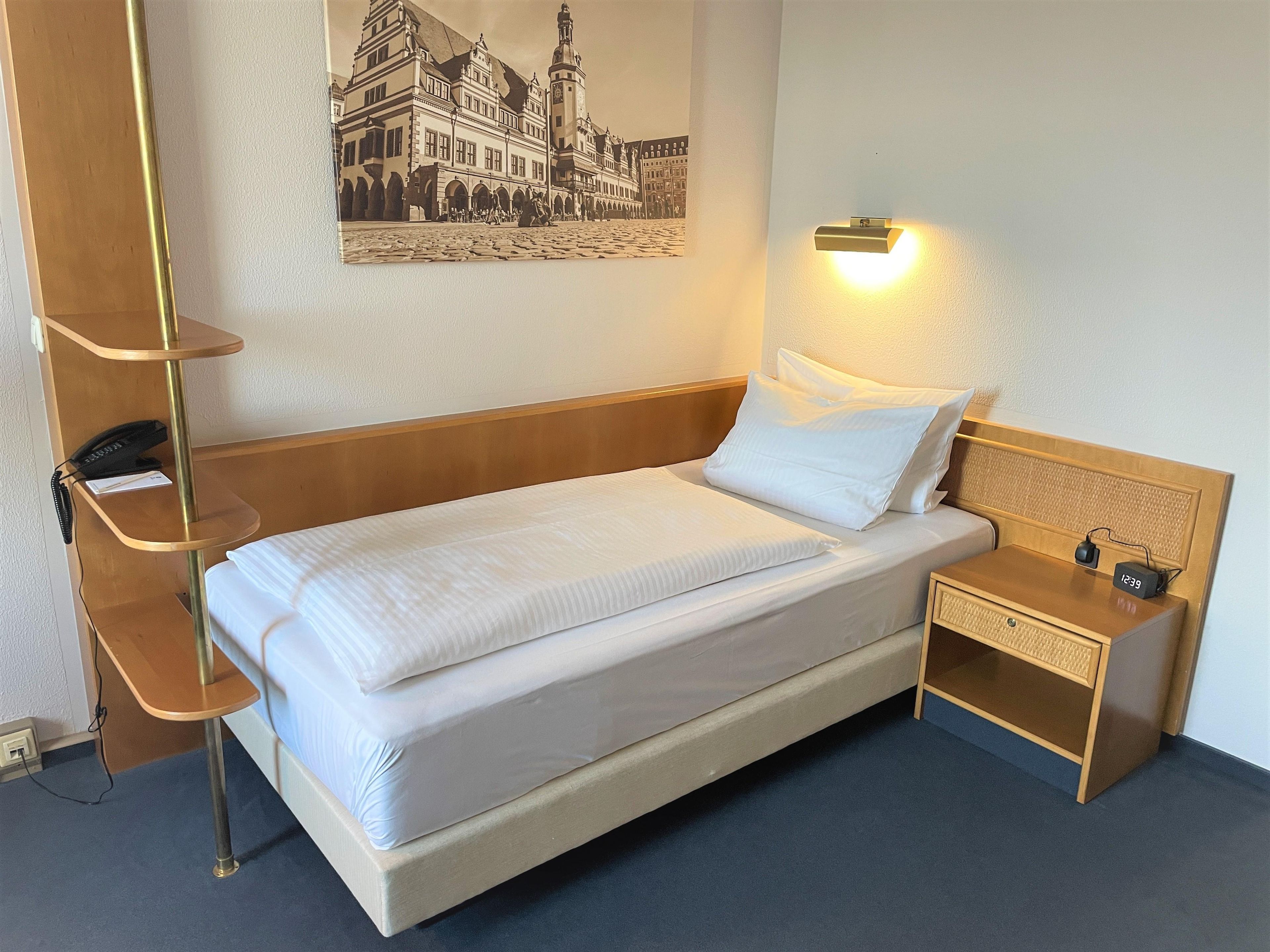 Habitación de hotel con una cama individual, mesita de noche, lámpara y teléfono instalado en la pared.
