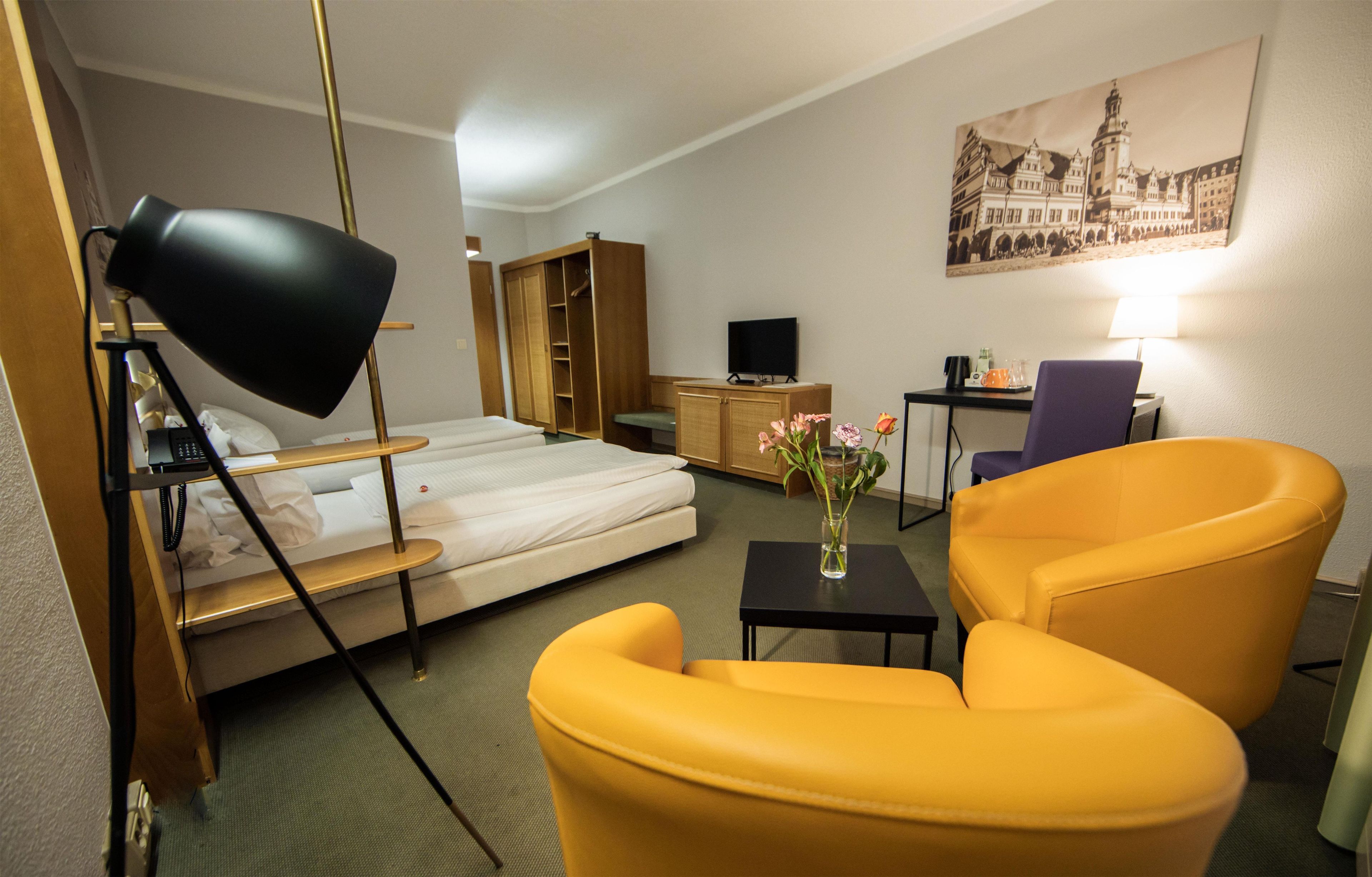 A hotel room with a bed, a desk, a chair, a lamp, a television, and a painting on the wall.