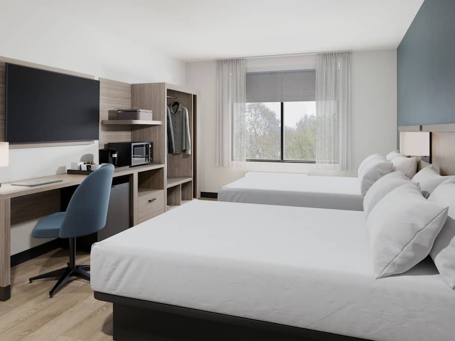 Quarto de hotel com cama, escrivaninha, cadeira e televisão.