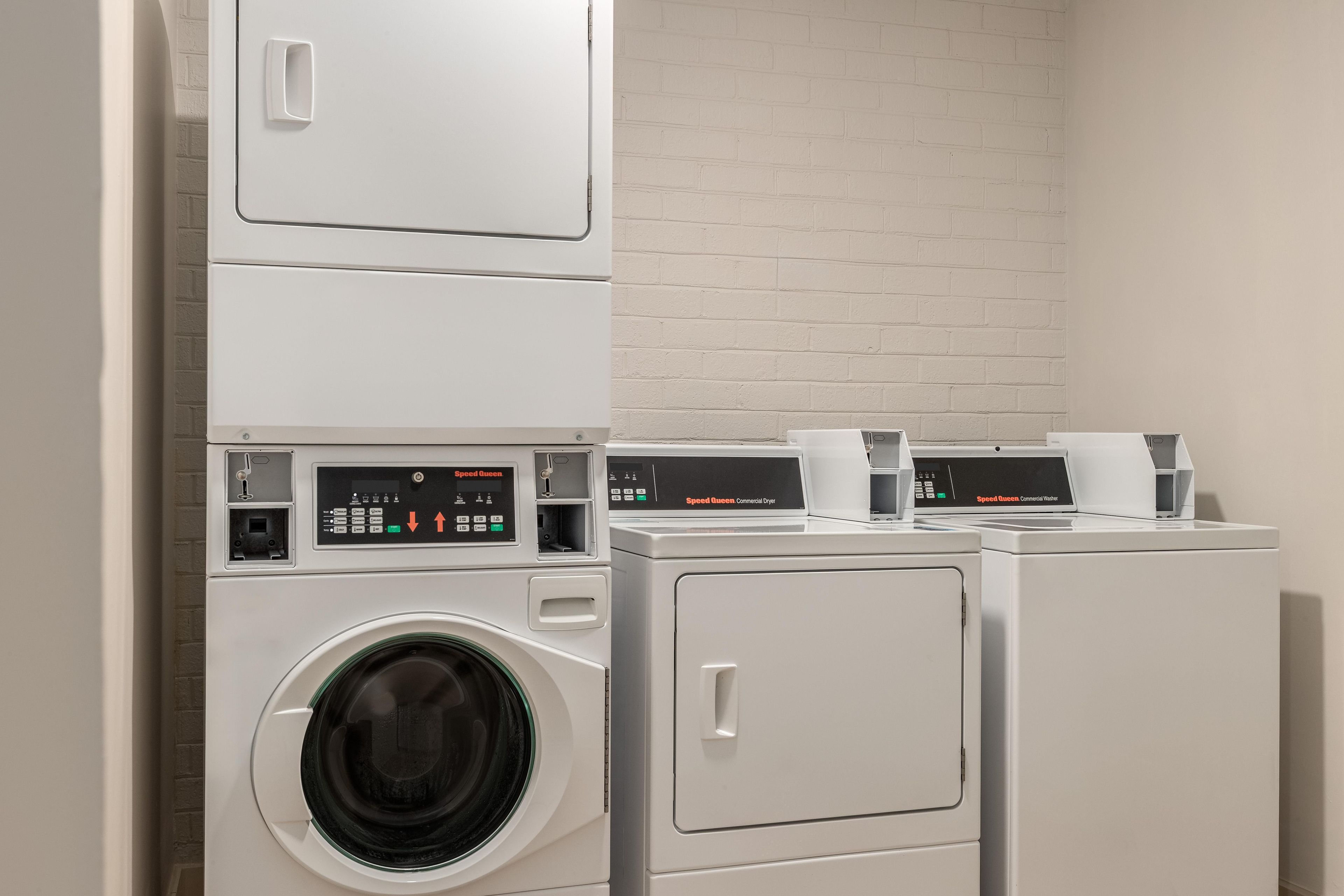 A laundry area with stacked washers and dryers, control panels, and a brick wall.