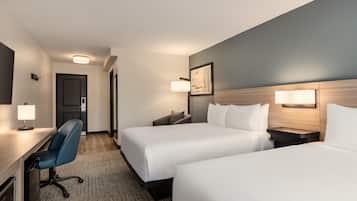 A hotel room with two beds, a desk, a chair, and a door.