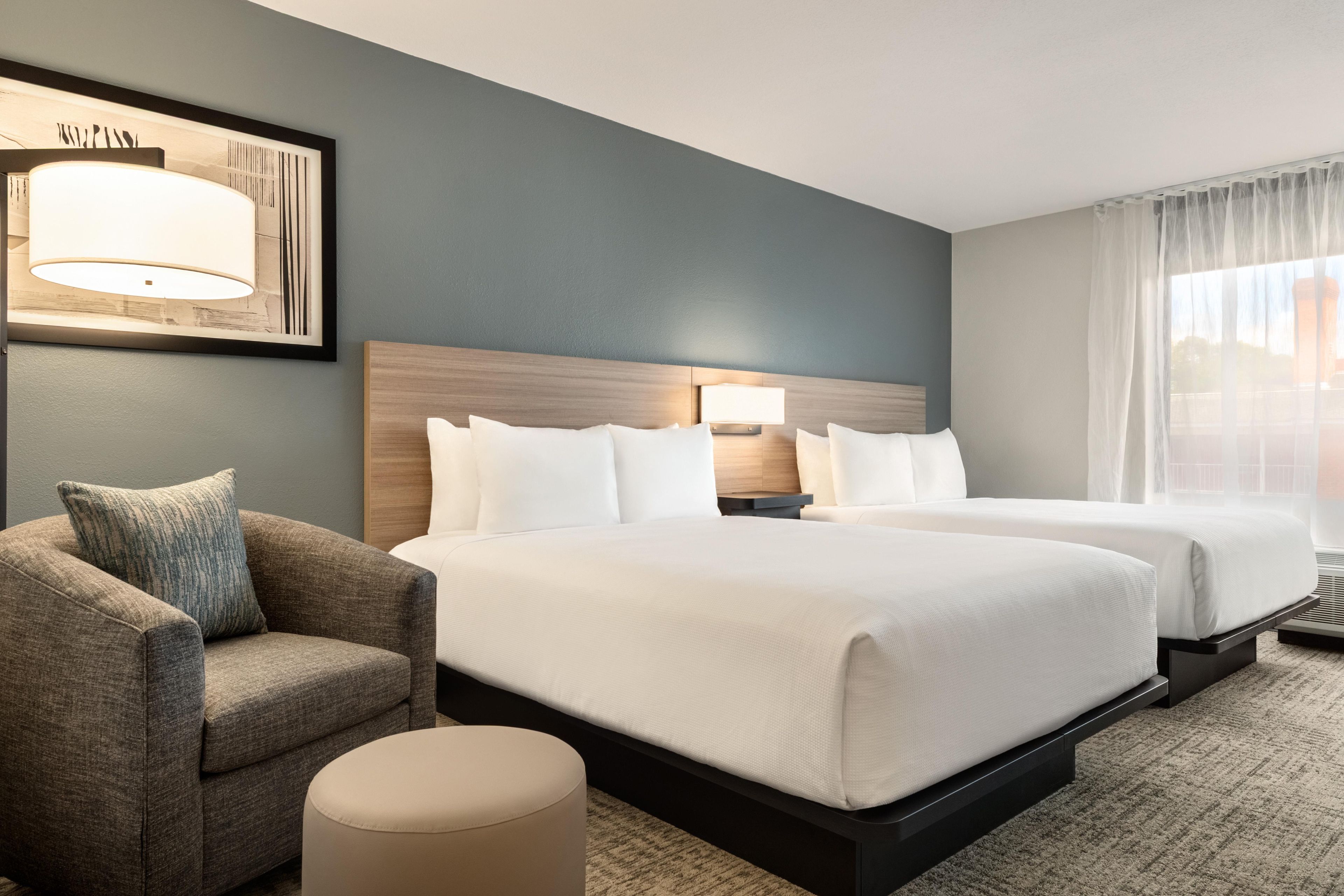 Une chambre d’hôtel avec deux lits, un canapé, une lampe et une fenêtre avec des rideaux.