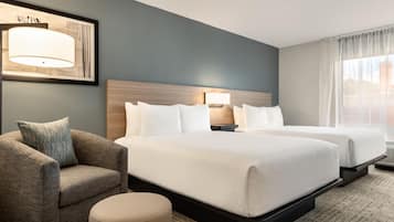 Une chambre d’hôtel avec deux lits, un canapé, une lampe et une fenêtre avec des rideaux.