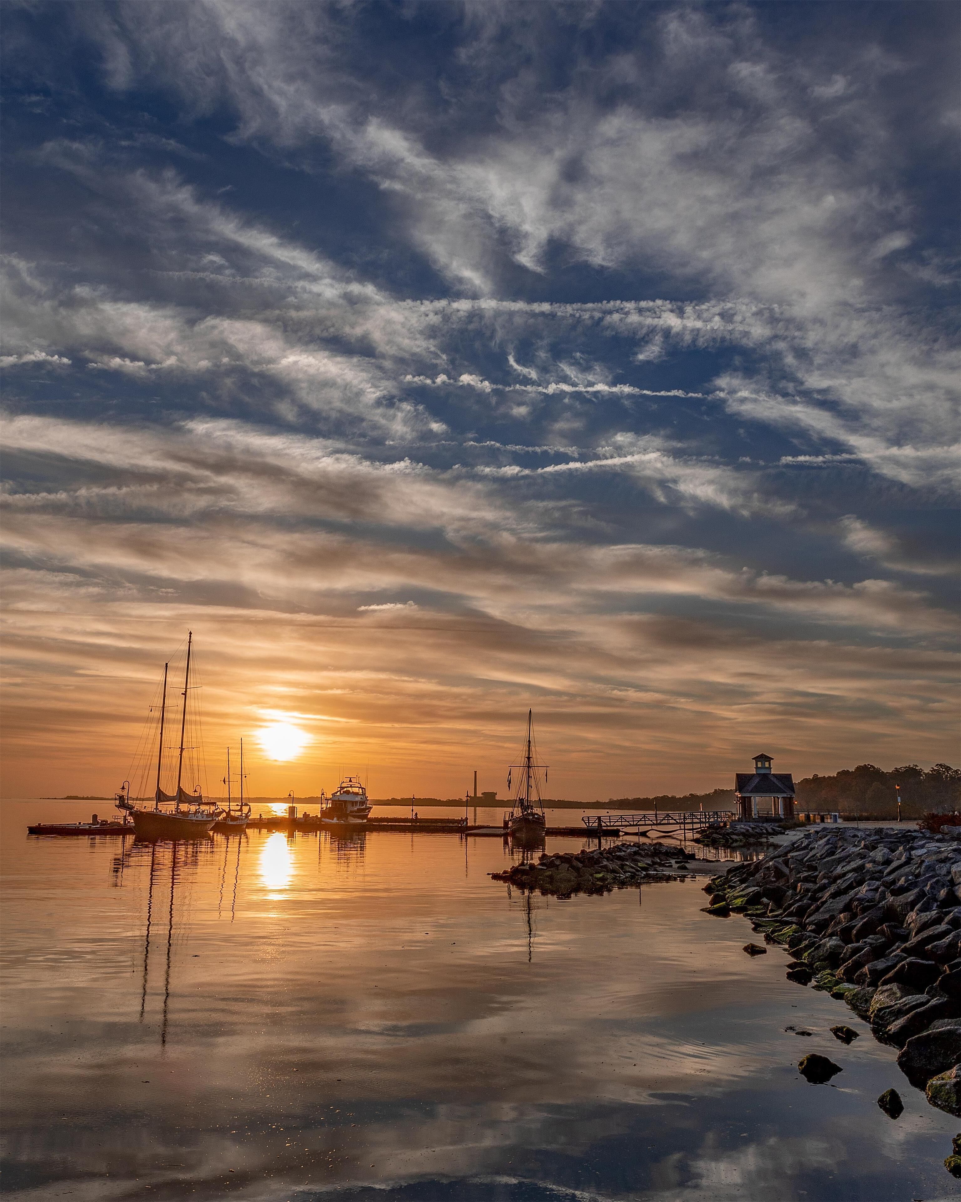 Un puerto tranquilo con barcos y un faro al atardecer.