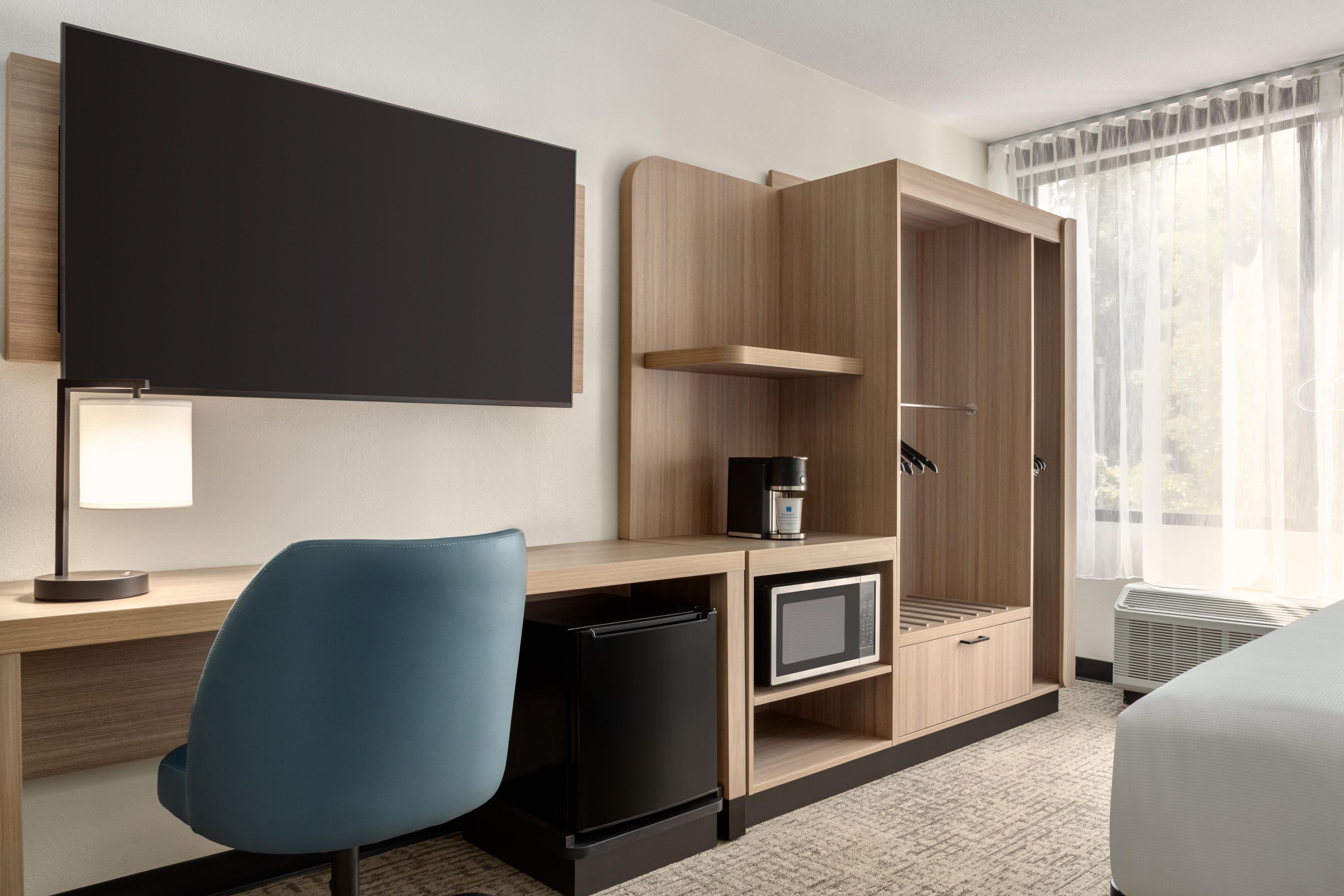 Une chambre d’hôtel équipée d’un bureau, d’une chaise, d’une télévision, d’une machine à café et d’une armoire.