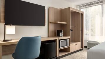 Una habitación de hotel con escritorio, silla, televisor, cafetera y armario.