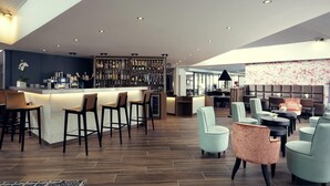 A modern bar area with a long counter, multiple bar stools, and a variety of bottles and glasses. - Mercure Orange Centre (Orange)