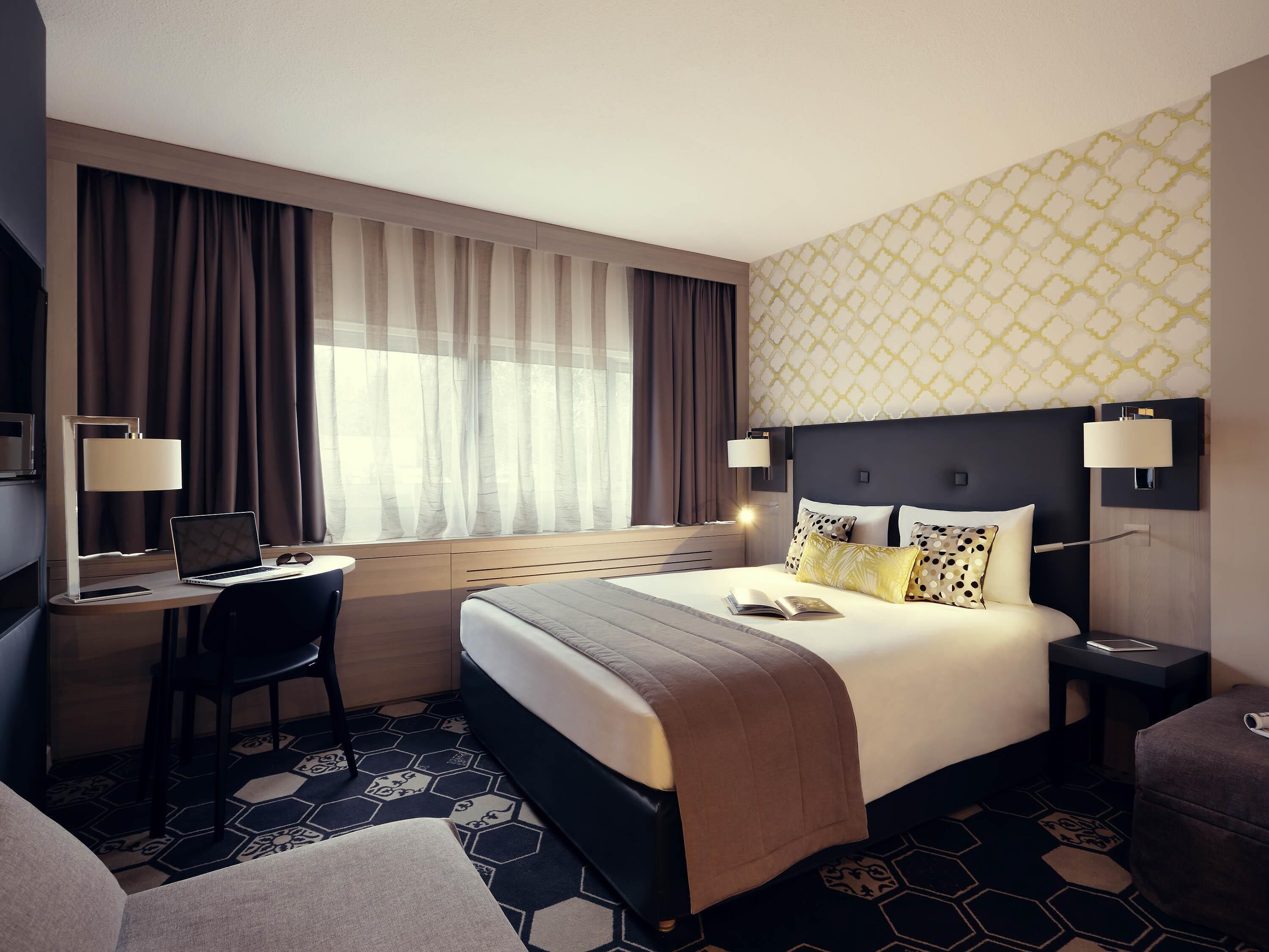 A hotel room with a bed, desk, chair, and a window with curtains.
