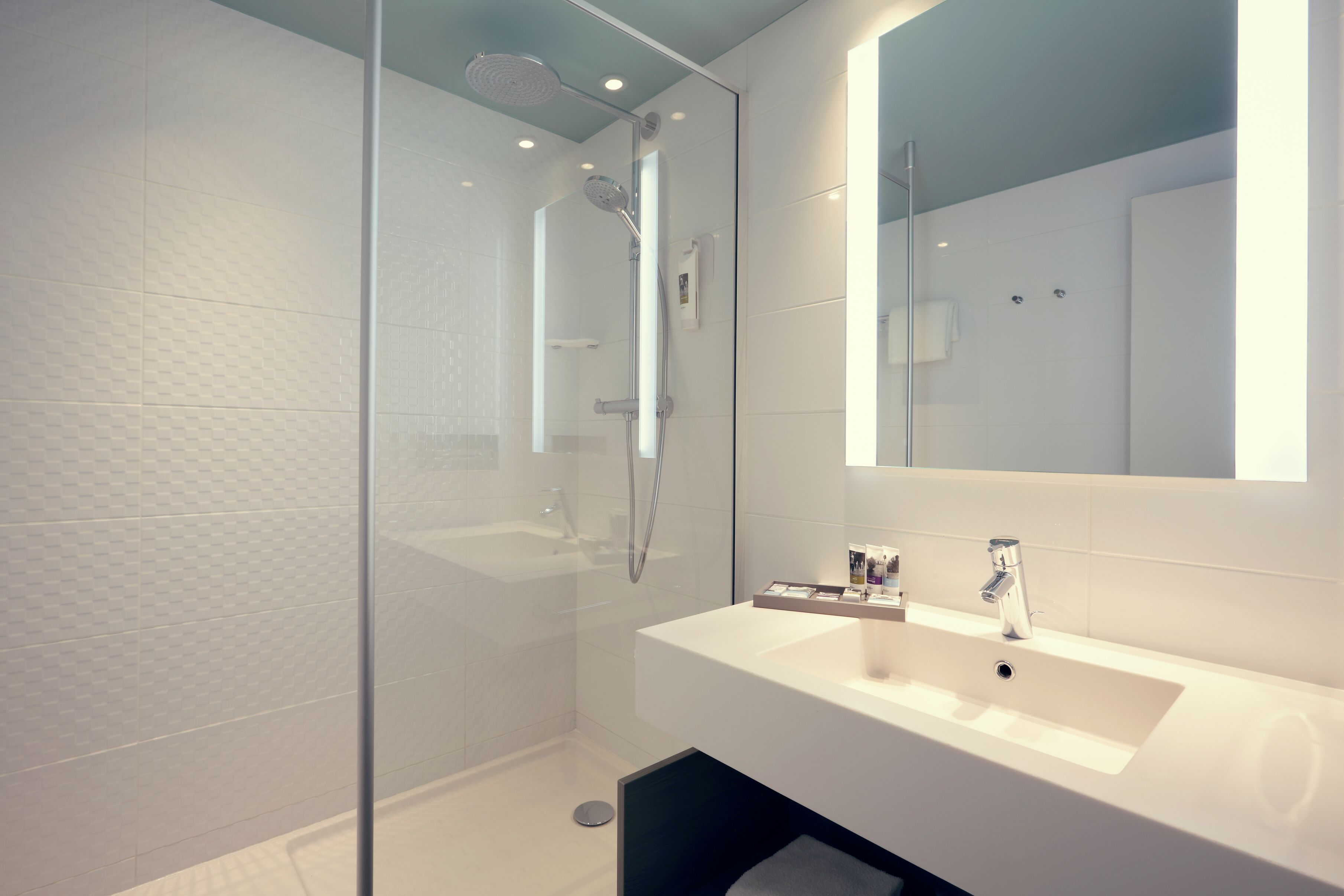 A modern bathroom with a glass-enclosed shower, a white sink, and a large mirror.