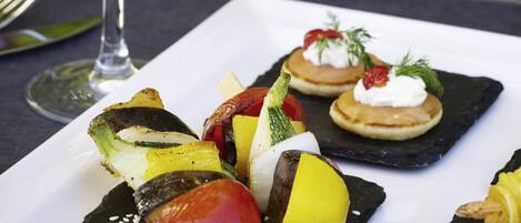 A square plate with skewered vegetables and a small dish with cream and herbs.