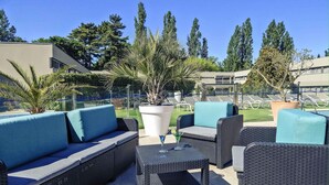 Outdoor patio furniture with cushions, a potted plant, and a clear view of a pool and lounge chairs in the background. - Mercure Orange Centre (Orange)