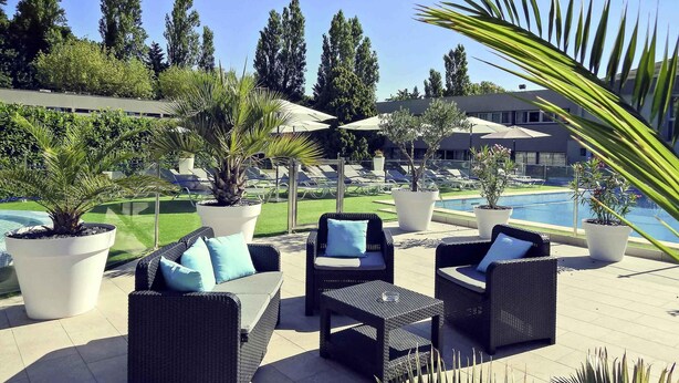 Outdoor seating with potted plants, a pool, and a building in the background. - Mercure Orange Centre (Orange)