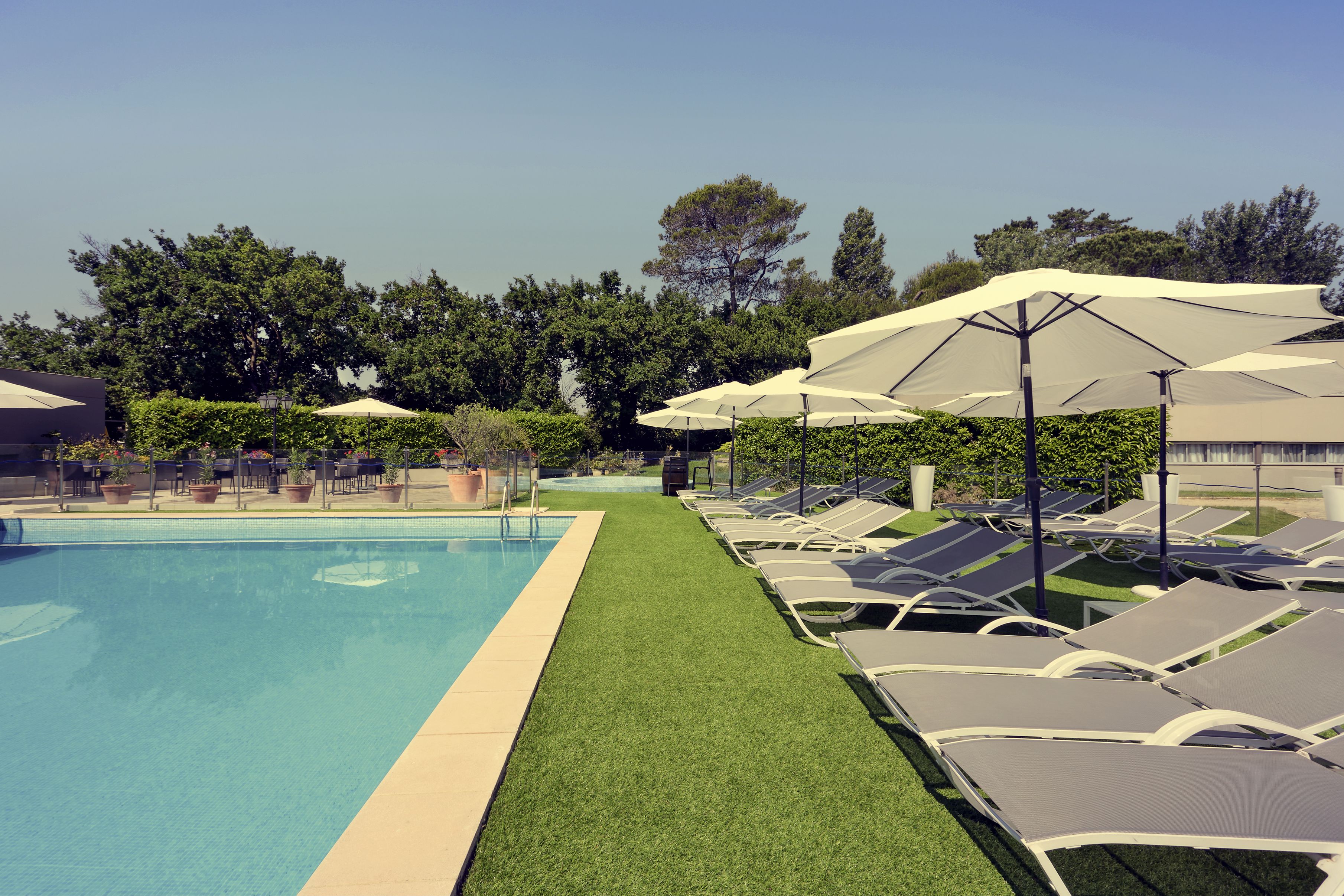 A swimming pool with a green lawn area, lounge chairs, and umbrellas.