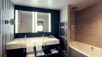 A modern bathroom with a large mirror, two sinks, a towel rack, and a bathtub.