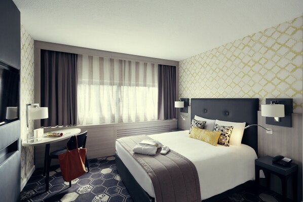 Una habitación de hotel con una cama, un escritorio, una silla, una ventana con cortinas y una pared con diseño.