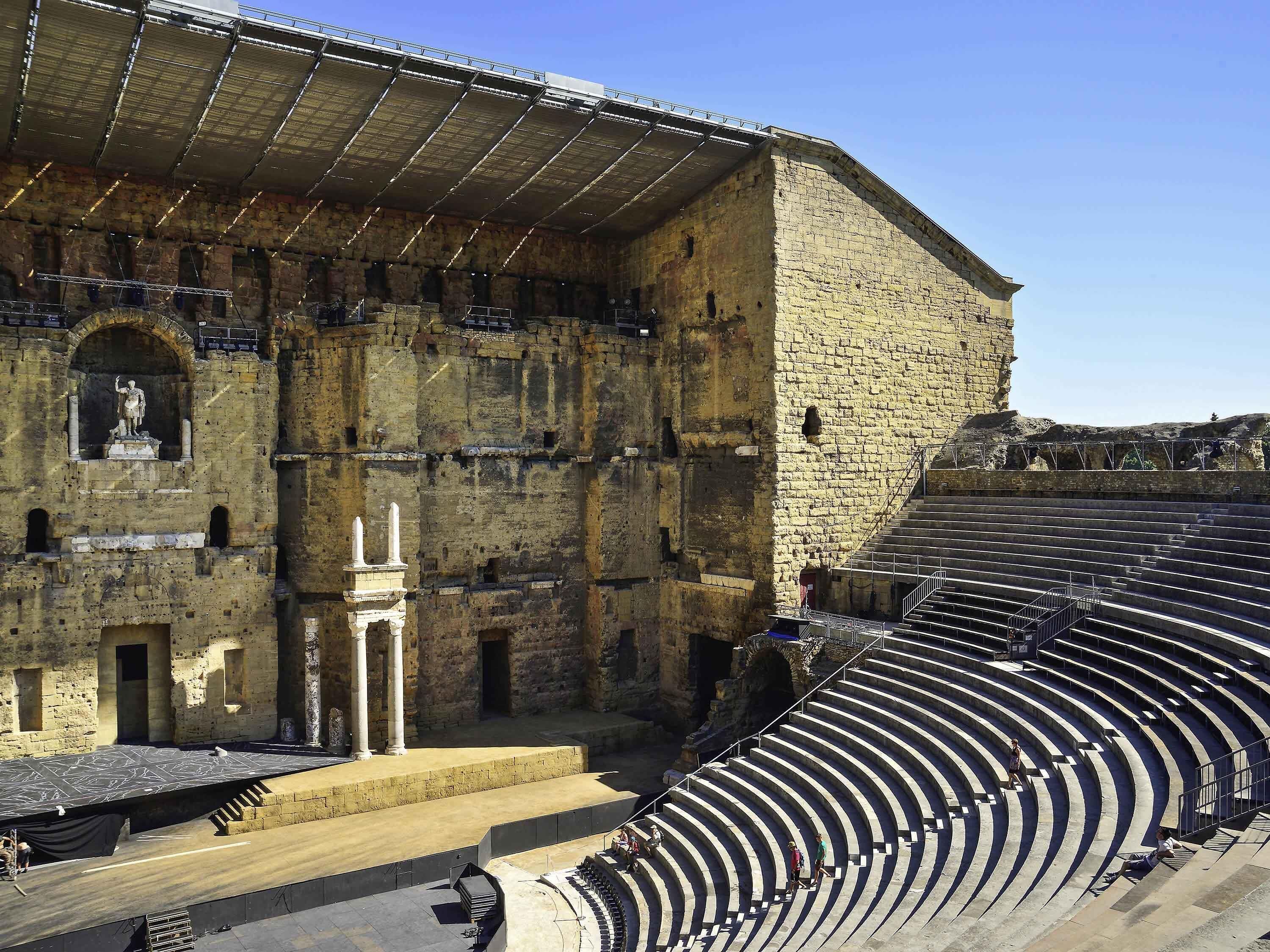 An ancient amphitheater with stone seating and a statue.