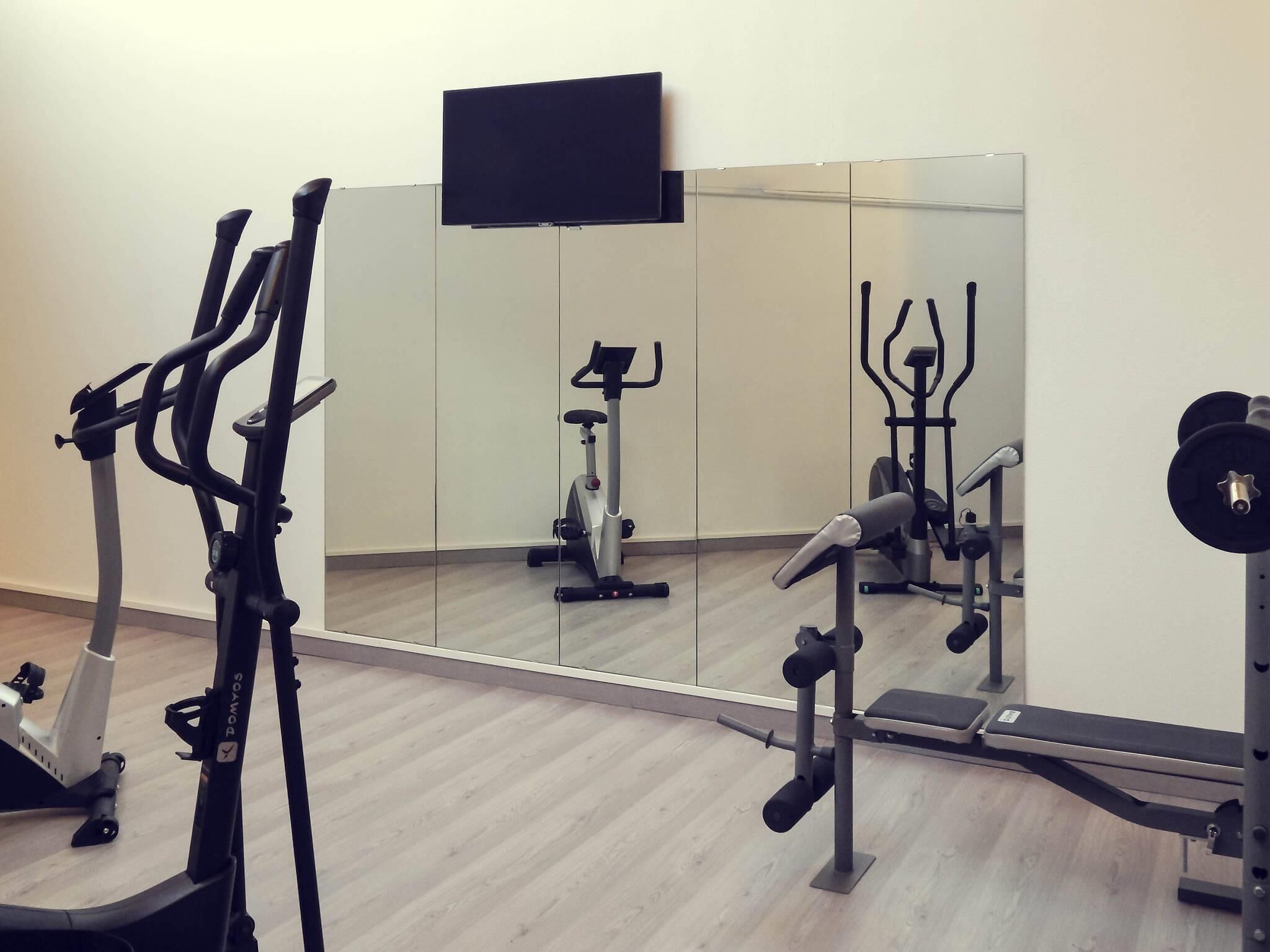 A gym with exercise equipment, a mirror, and a TV on the wall.