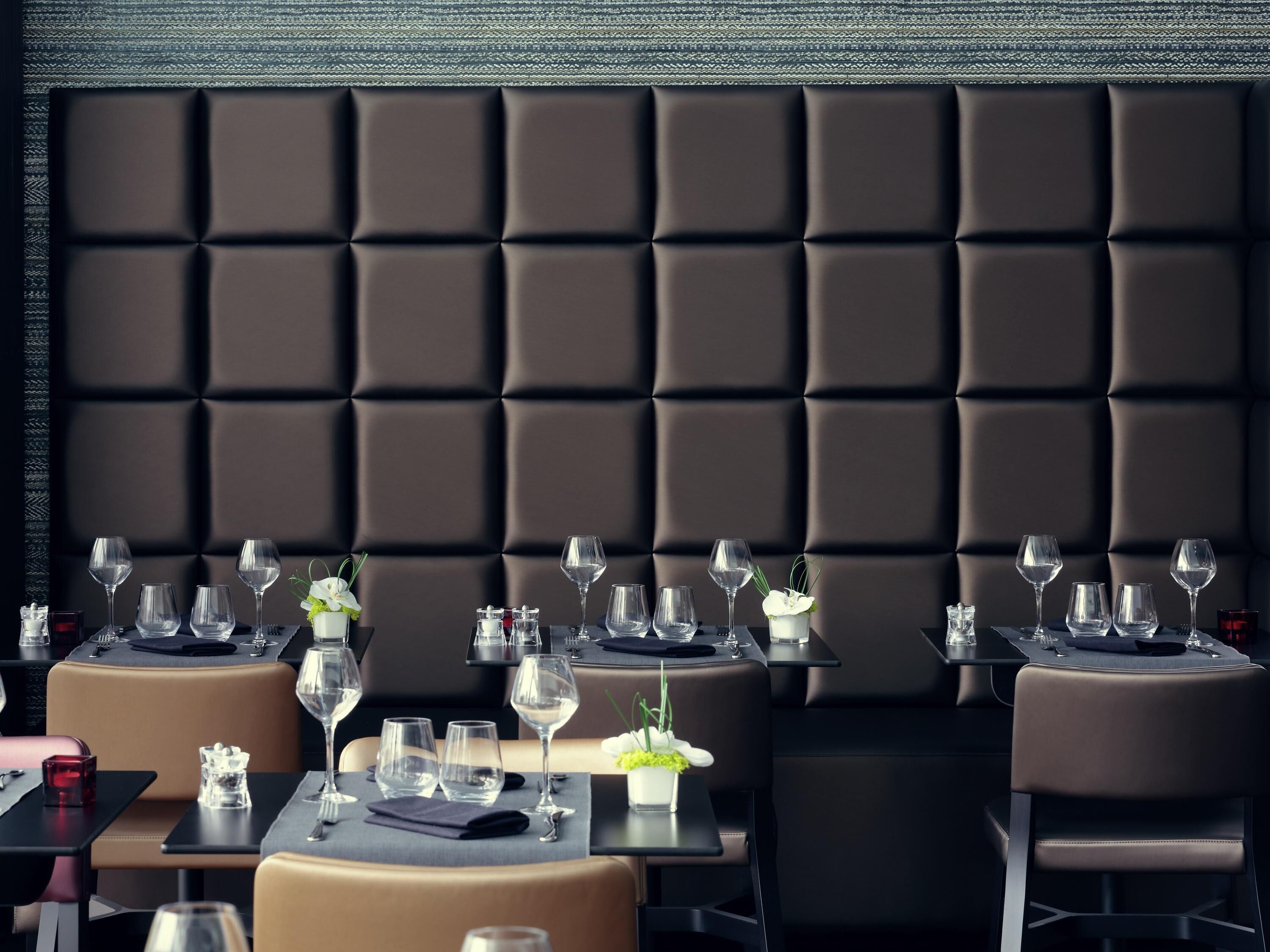 En restaurant med mørk, polstret væg og borde dækket med vinglas og bestik.