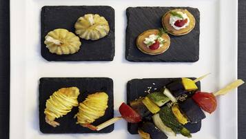 A square white plate with four square black slate tiles, each containing different food items.