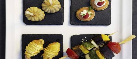 Un plato blanco cuadrado con cuatro baldosas negras de pizarra, cada una con diferentes alimentos.