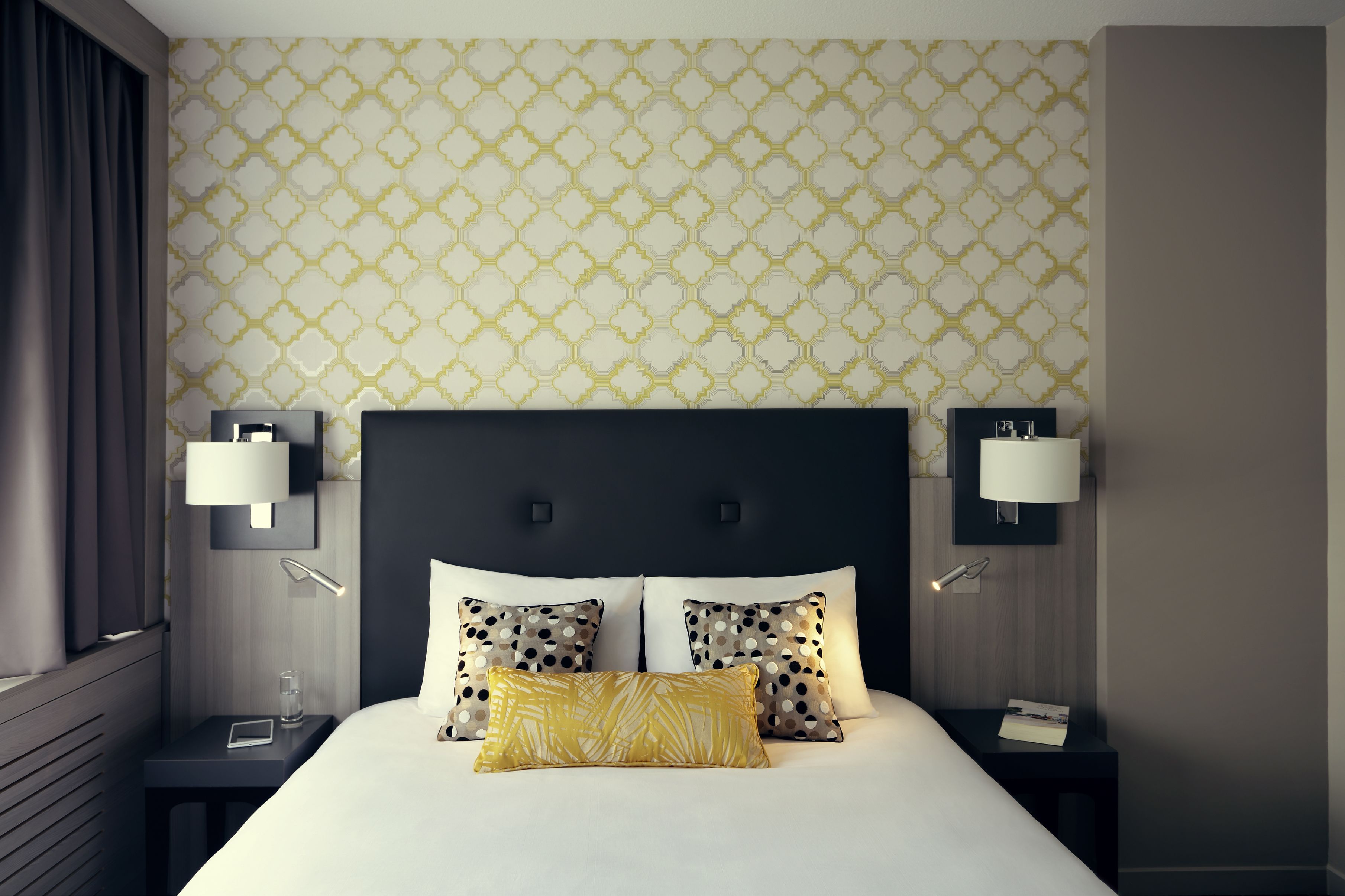 Habitación de hotel con una cama grande, dos mesitas de noche, una lámpara de pared y un papel tapiz estampado.